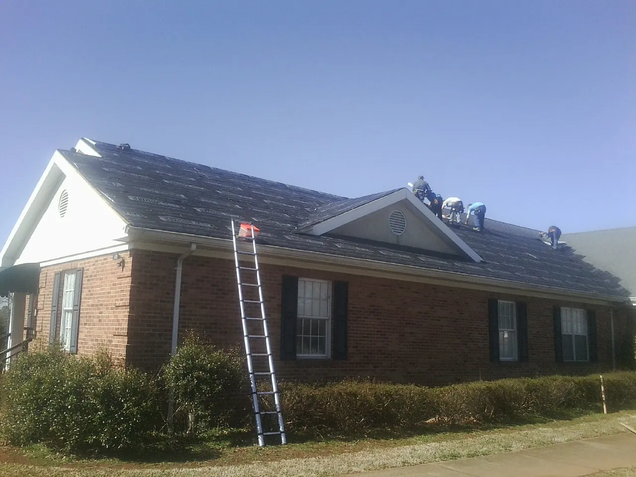 Crew tearing shingles off a brick ranch roof with a ladder set — Metal Roof Repair work by our crew in Walnut